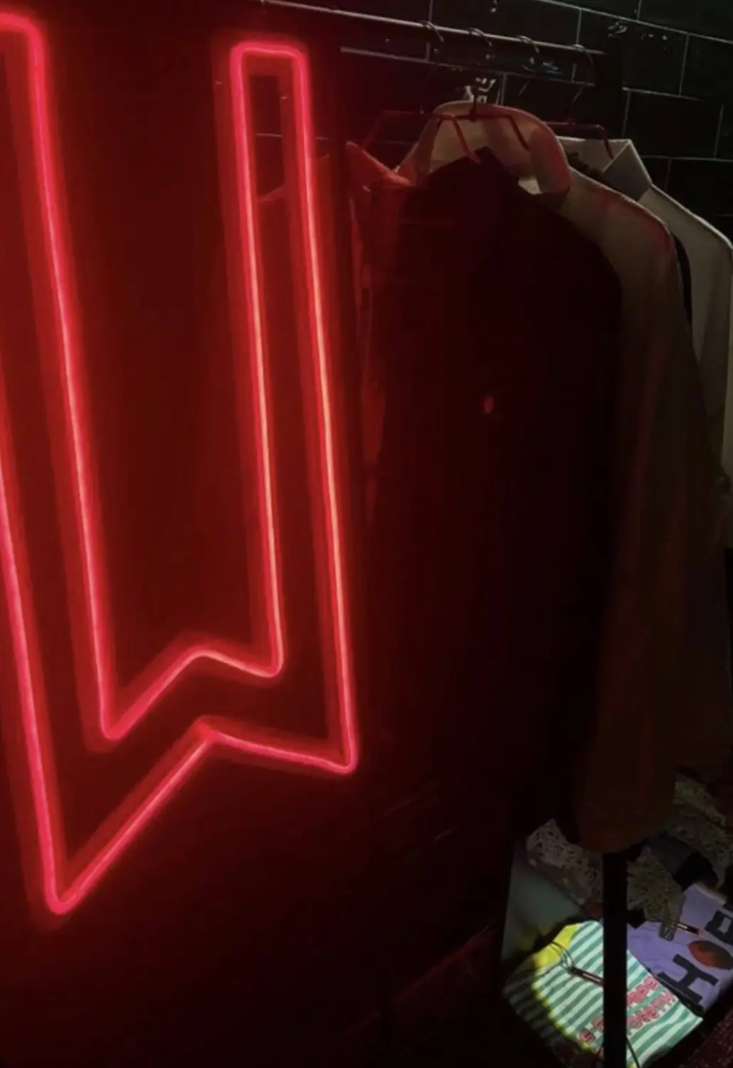 Red neon logo sign glowing beside a clothing rail in the What Remains store