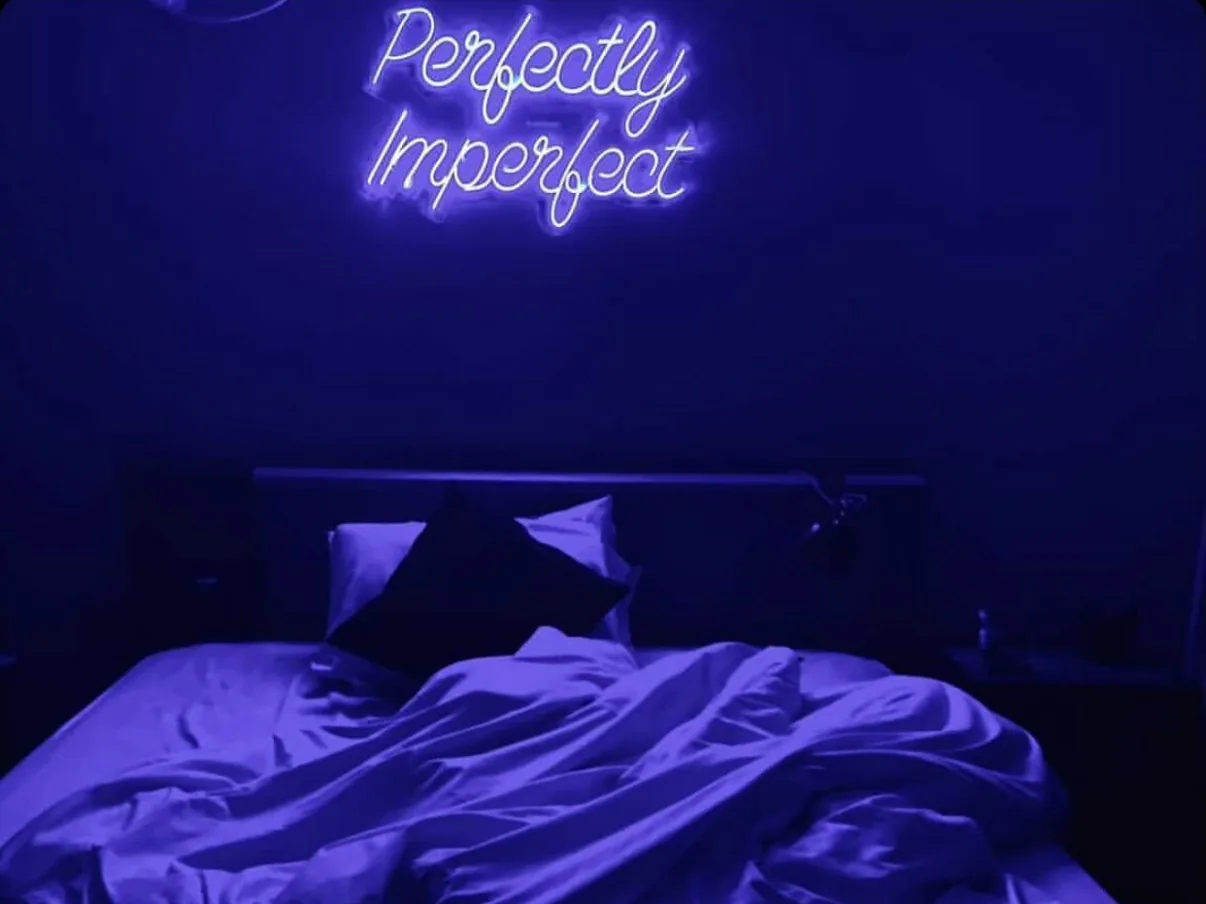 Perfectly Imperfect script neon in blue above a bed